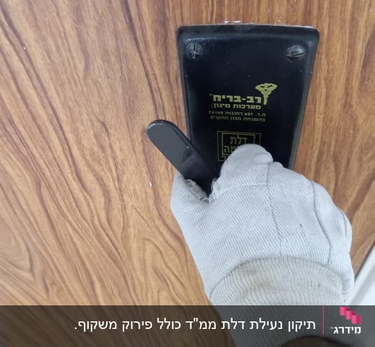 יד עם כפפה מחזיקה ידית דלת על רקע עץ